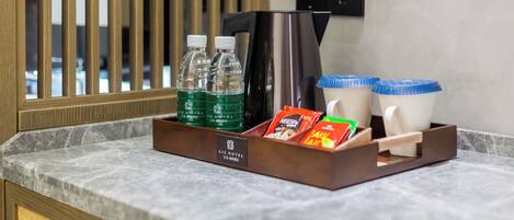 A hotel room's minibar with bottled water, coffee maker, and disposable cups.