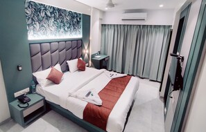 A hotel room with a large bed, a bedside table with a phone, a small table with a lamp, and a view of the outside through curtains. - Hotel Everest Residency (Navi Mumbai)