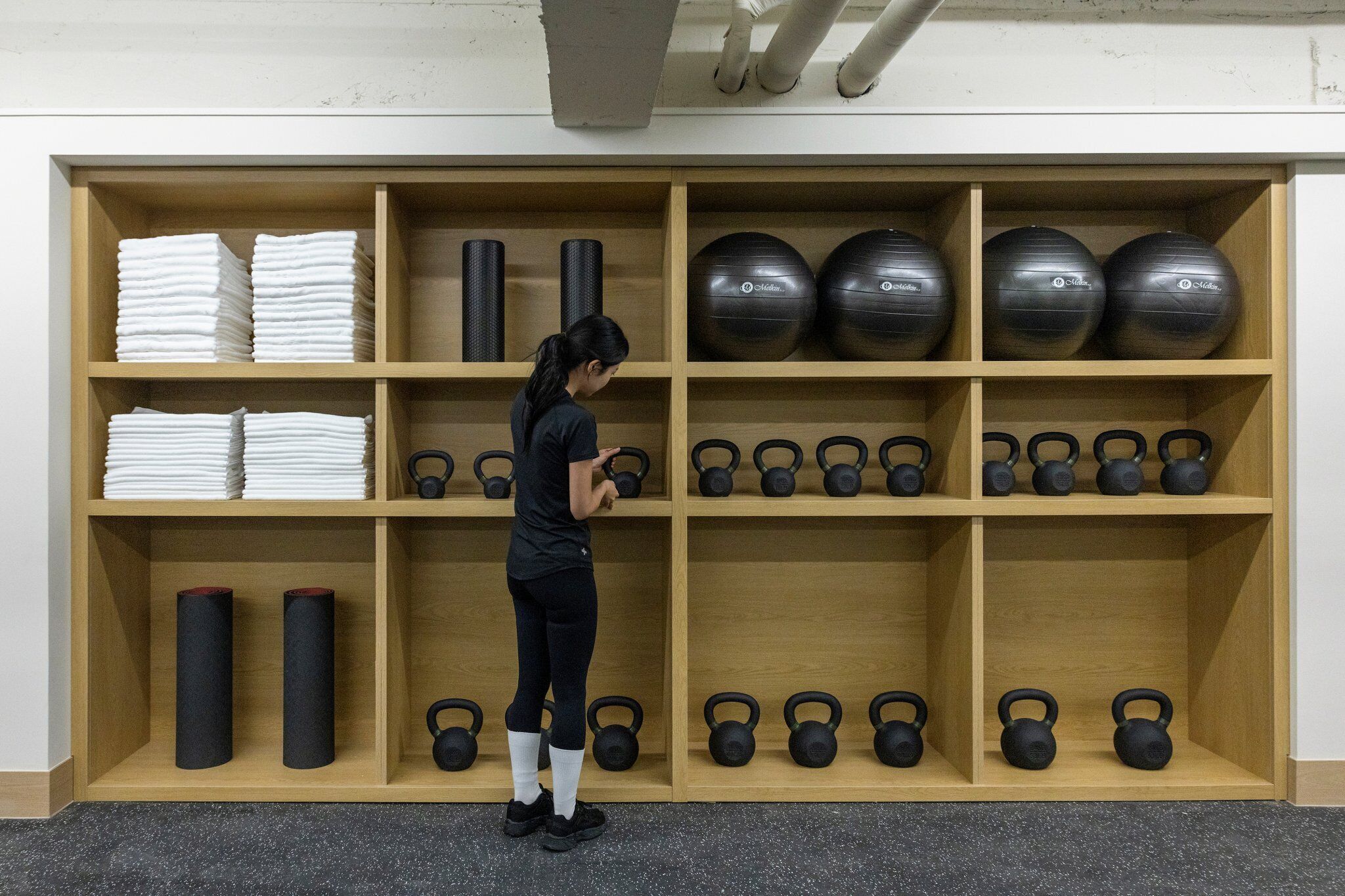 Ein Fitnessraum mit Holzböden und Regalen, die Handtücher, Yogamatten, Kettlebells und Gymbälle beherbergen.