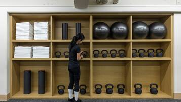 Ein Fitnessraum mit Holzböden und Regalen, die Handtücher, Yogamatten, Kettlebells und Gymbälle beherbergen.