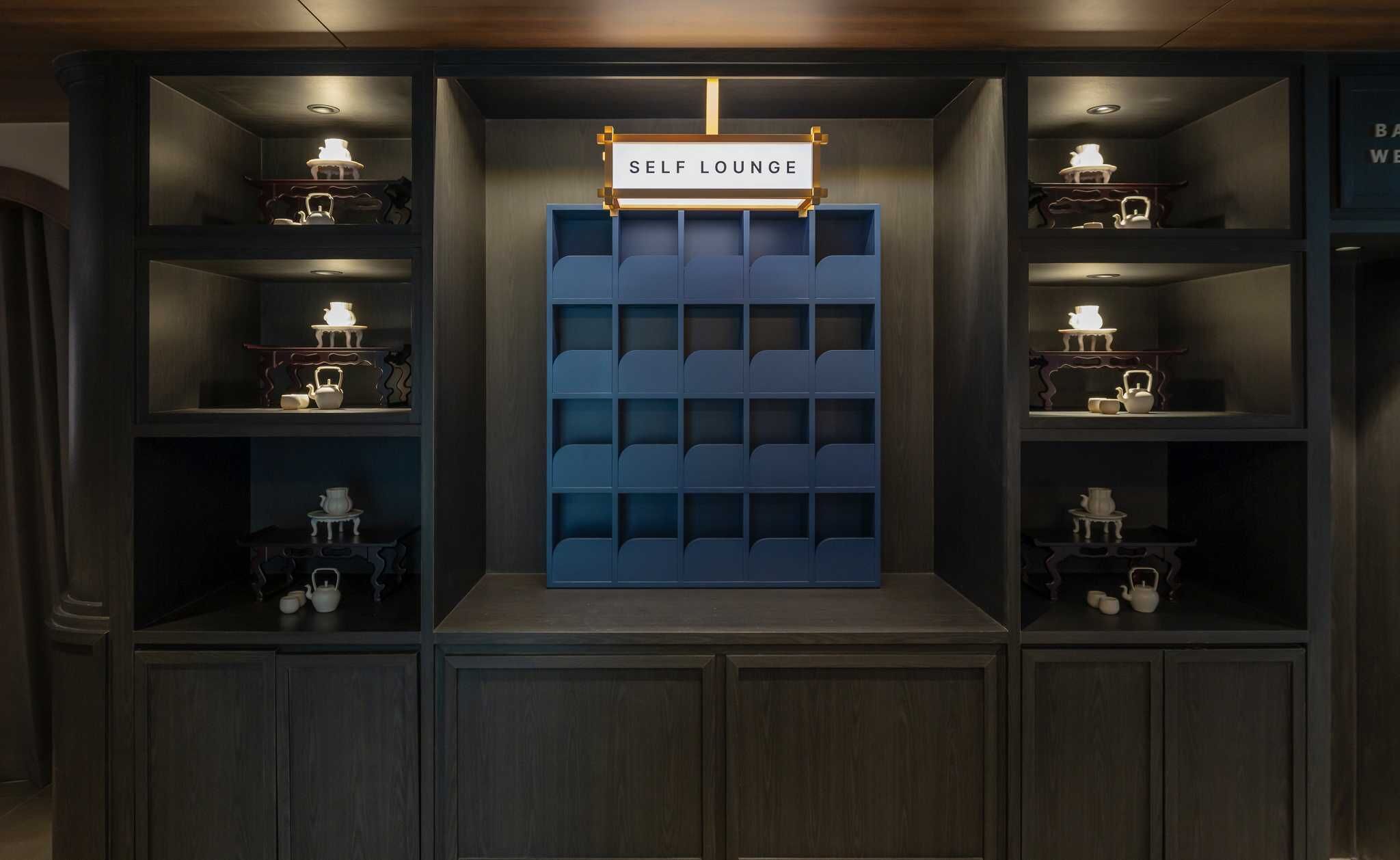A self-lounge area with a blue seating wall and shelves with tea sets.