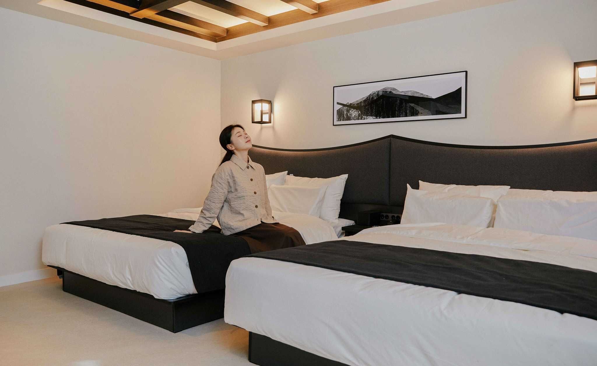 Ein Hotelzimmer mit zwei Betten, einem großen Bett links und einem kleineren rechts. Darüber an der Wand hängt ein Bild.
