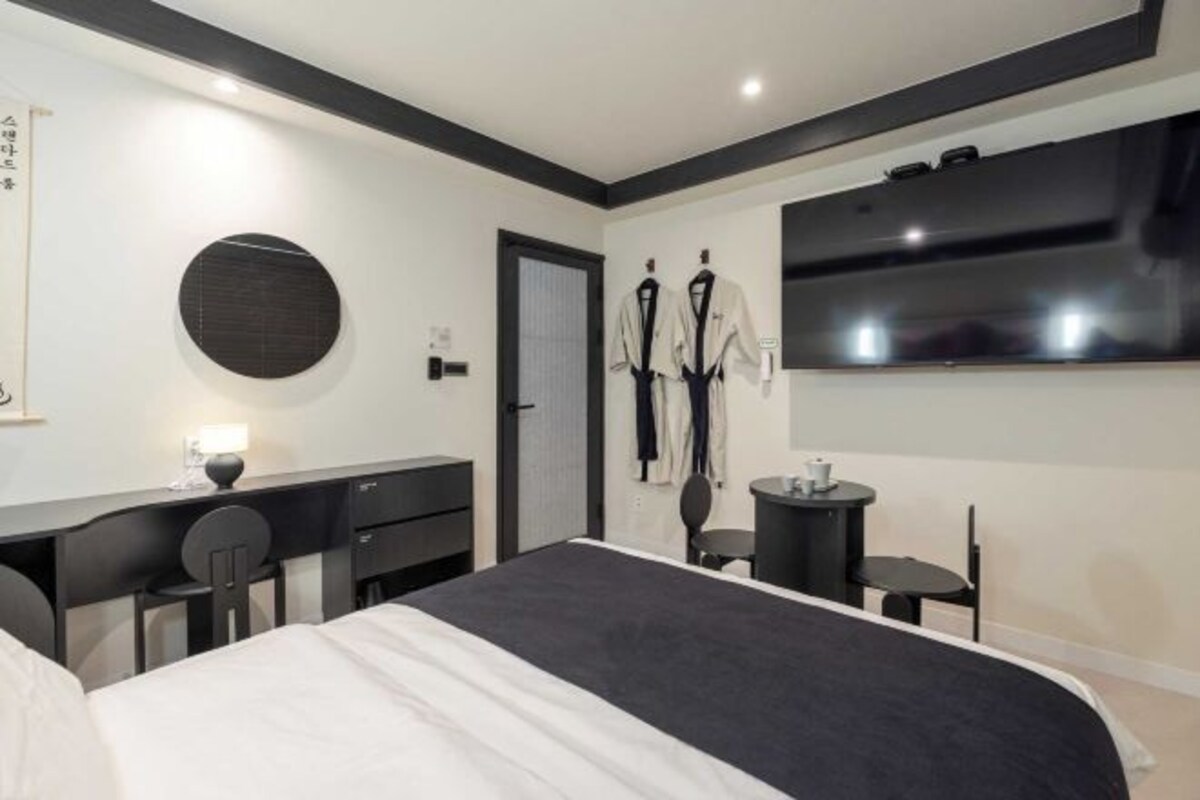 Una habitación de hotel moderna con una cama grande, un escritorio con una silla, una mesita con una silla y un televisor montado en la pared.