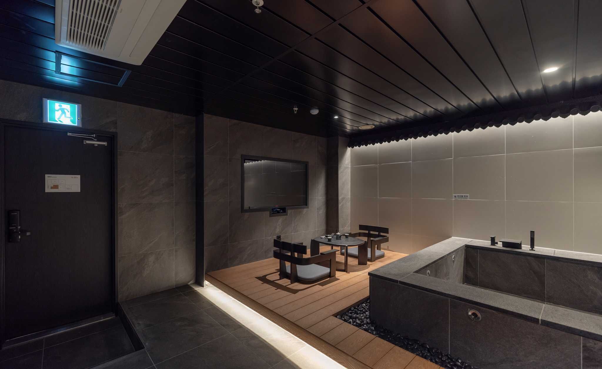 A modern bathroom with a large bathtub, a wooden floor, and a flat-screen TV mounted on the wall.
