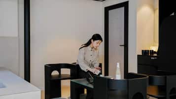 A modern hotel room with a minimalist design, featuring a large bed, a desk with a chair, and a small table with a bottle and cup.