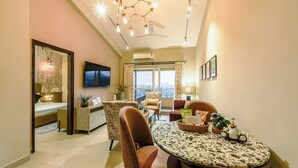 A modern living room with a dining area, a TV mounted on the wall, and a balcony with a view. - Alaya Stays Veera Serina 3 BHK with Pool (Candolim)