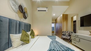 A modern hotel room with a large bed, a flat-screen TV, a wardrobe, and a seating area. - Alaya Stays Veera Serina 3 BHK with Pool (Candolim)