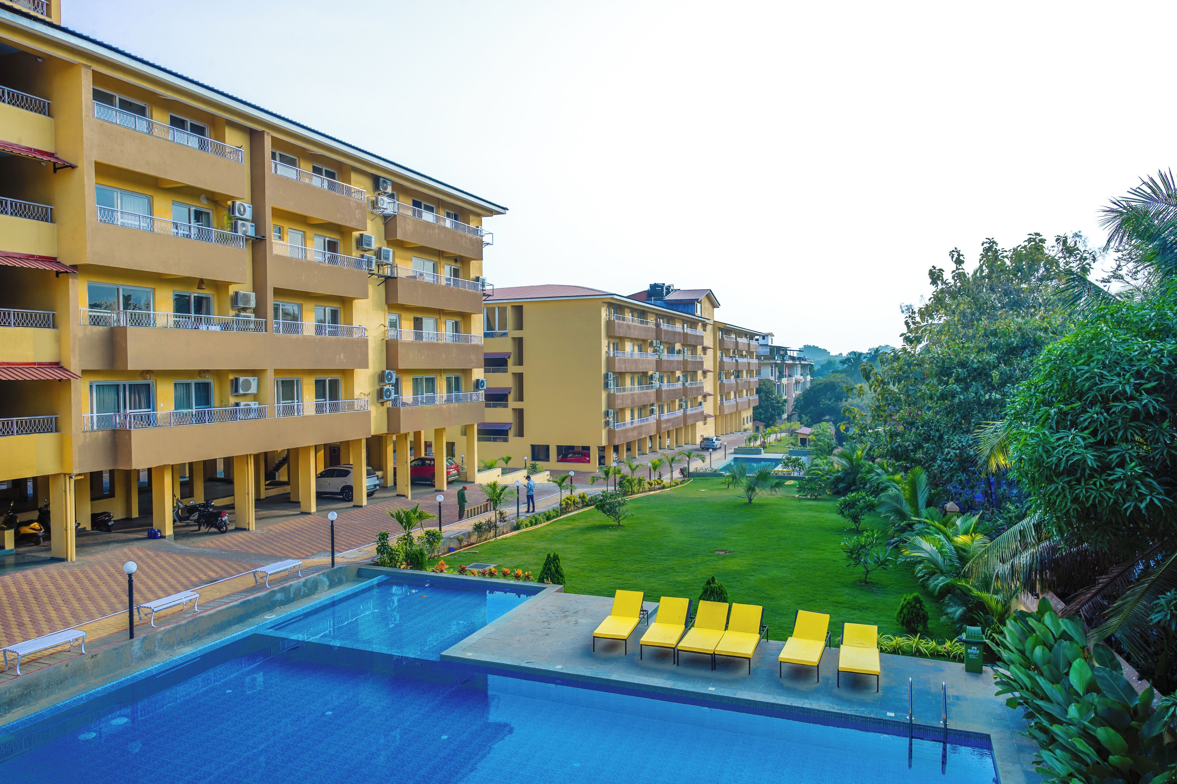 A hotel with multiple balconies, a swimming pool, and a well-maintained lawn area.