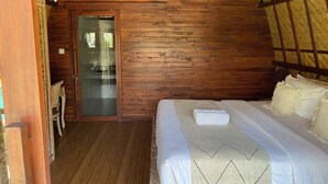 Een kamer met houten wanden, een bed met wit beddengoed, een houten deur en een kleine tafel met stoelen.