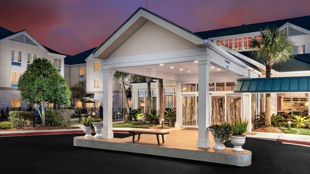 A hotel entrance with a covered patio, outdoor seating, and potted plants. - Wyndham Garden NEW Orleans Airport (Kenner)