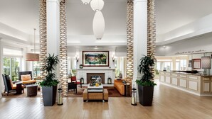 A spacious living area with a fireplace, comfortable seating, and decorative lighting. - Wyndham Garden NEW Orleans Airport (Kenner)