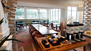 A spacious dining area with multiple tables and chairs, a coffee station with dispensers, and a view of the outdoors through large windows. - Wyndham Garden NEW Orleans Airport (Kenner)