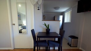 Un comedor con una mesa, sillas, una planta en maceta, un ventilador de pared, un espejo y un televisor.