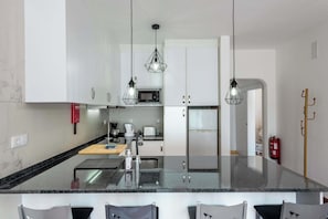 A modern kitchen with white cabinets, a granite countertop, and pendant lighting.