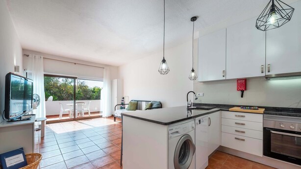 A compact kitchen with a washing machine, a dining area with a table and chairs, and a television. - Pateo Apartment - One Bedroom in Albufeira (Albufeira)