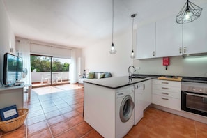 A compact kitchen with a washing machine, a dining area with a table and chairs, and a television.