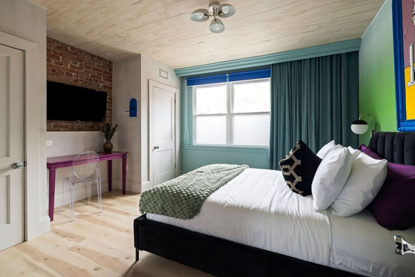 Un dormitorio con cama, escritorio, televisor y ventana con cortinas.