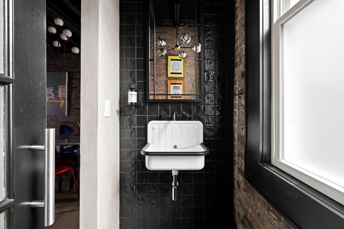 Ein schmales Badezimmer mit einem weißen Waschbecken, schwarzen Fliesenwänden und einer Wand mit Ziegeln.
