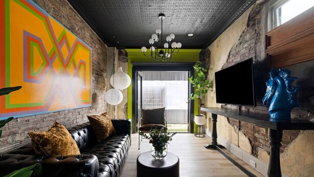 A modern living room with a black leather sofa, a round coffee table, and a large abstract painting on the wall. - 258 38th St. - Brownstone (Pittsburgh)