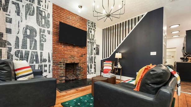 A modern living room with a brick fireplace, black sofas, and a staircase leading to another level.