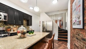 A kitchen with dark cabinets, a granite countertop, a glass jar with baseballs, and a stainless steel refrigerator.