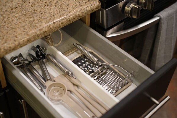 Un cajón con utensilios de cocina, como un rallador, un batidor y unas pinzas.