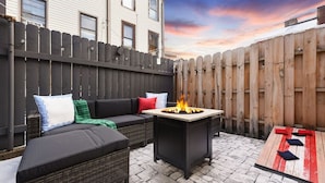 A backyard with a black outdoor sofa, a small fire pit, and a wooden table.