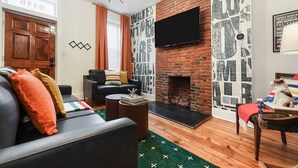 A living room with a fireplace, a sofa, a television, and a dog on a chair.