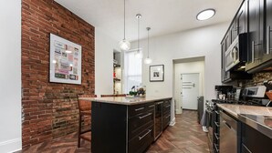 A kitchen with a brick accent wall, a central island with a sink, and modern cabinetry.