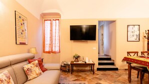 Un saló amb un sofà, una televisió, una taula de dinar amb caires i una escala que condueix a una altra habitació.