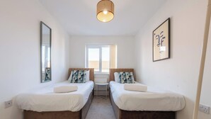 Habitación de hotel con dos camas individuales, un ventanal grande, un espejo, una lámpara en el techo y un cuadro en la pared.