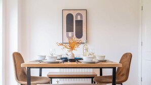 Una mesa de comedor con sillas, un florero con hojas secas y una botella de vino.