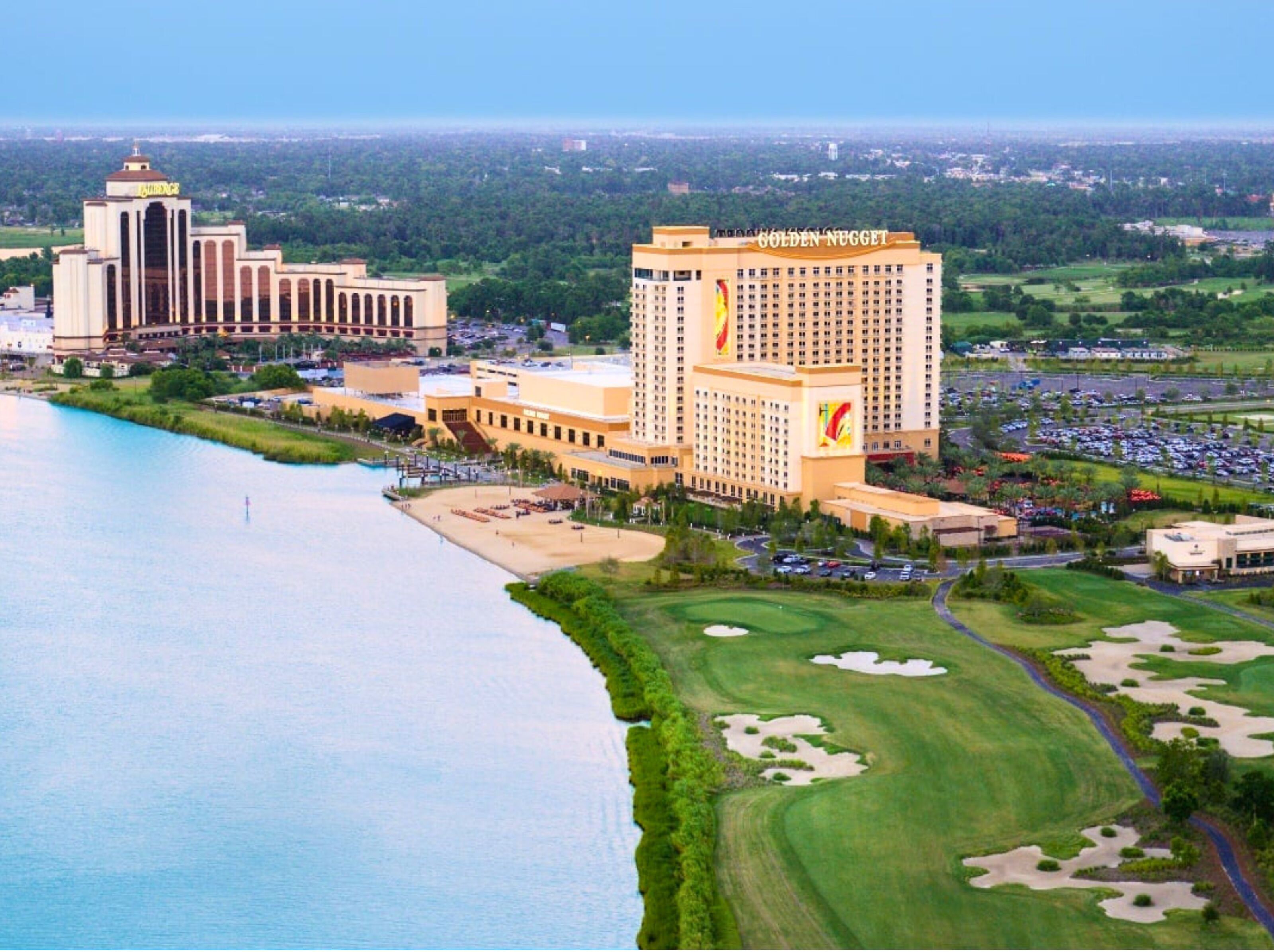 A large hotel with multiple buildings, including a prominent Golden Nugget sign, situated near a body of water with a golf course and parking area.