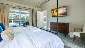A bedroom with a large bed, a ceiling fan, a wooden dresser, and a view of a pool and outdoor seating area. - Private Coastal Getaway to Connect and Celebrate (Palm Harbor)