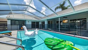 A swimming pool with a glass-enclosed roof, a swan float, and a large green leaf float. - Private Coastal Getaway to Connect and Celebrate (Palm Harbor)