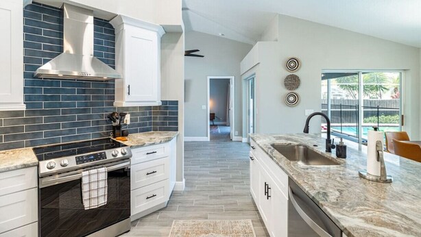 A modern kitchen with a large island, stainless steel appliances, and a view to a backyard. - Private Coastal Getaway to Connect and Celebrate (Palm Harbor)