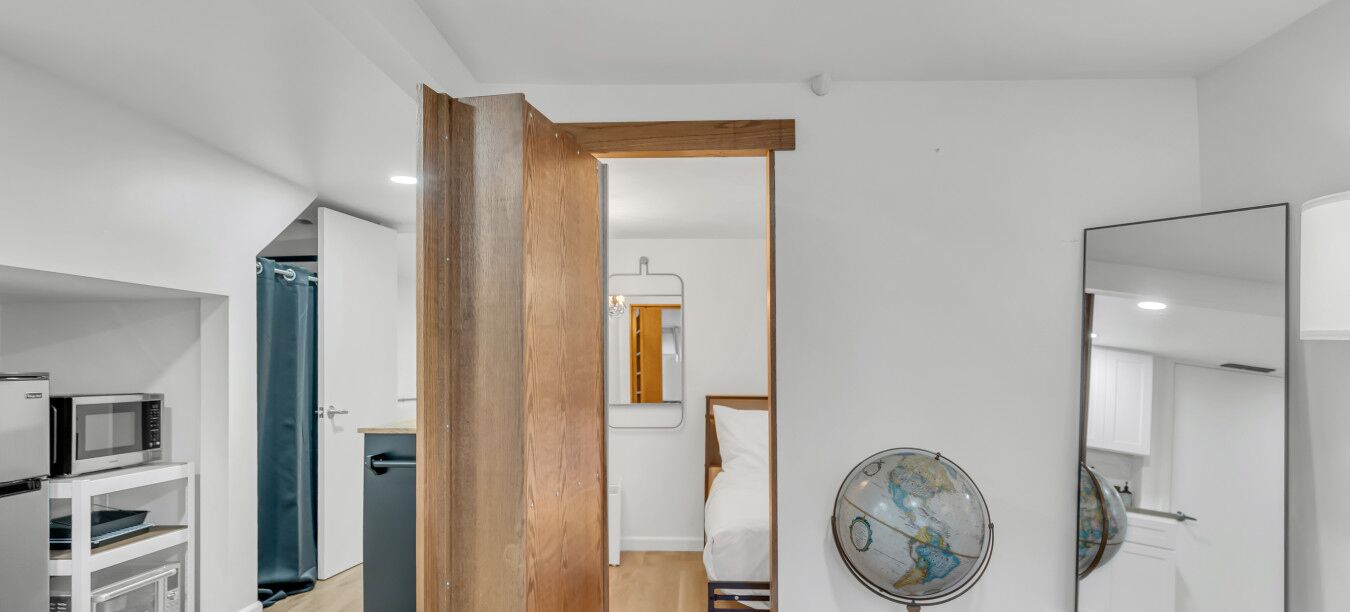 Habitación de hotel moderna con una puerta de madera, un globo en la pared, microondas y una pequeña cocina americana.