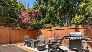 Un jardin avec une clôture en bois, un barbecue et un espace salon extérieur.