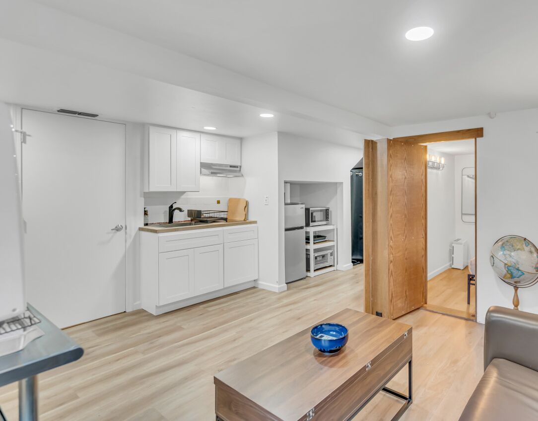 A modern kitchen with white cabinets, a dining table with a blue bowl, and a wooden door leading to another room.