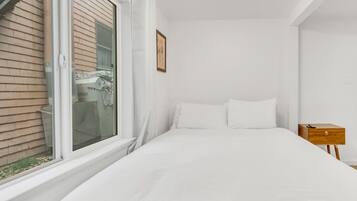 A bedroom with a bed, a window, a nightstand, and a wall-mounted light fixture.