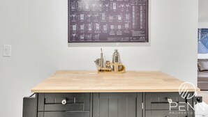 Un coin cuisine doté d’un plan de travail en bois, d’un graphique à barres fixé au mur et d’un ensemble d’ustensiles de bar.