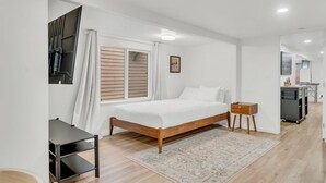 Une chambre à coucher comprenant un lit, une table de chevet, un bureau, une commode, une fenêtre avec des stores et un luminaire au plafond.