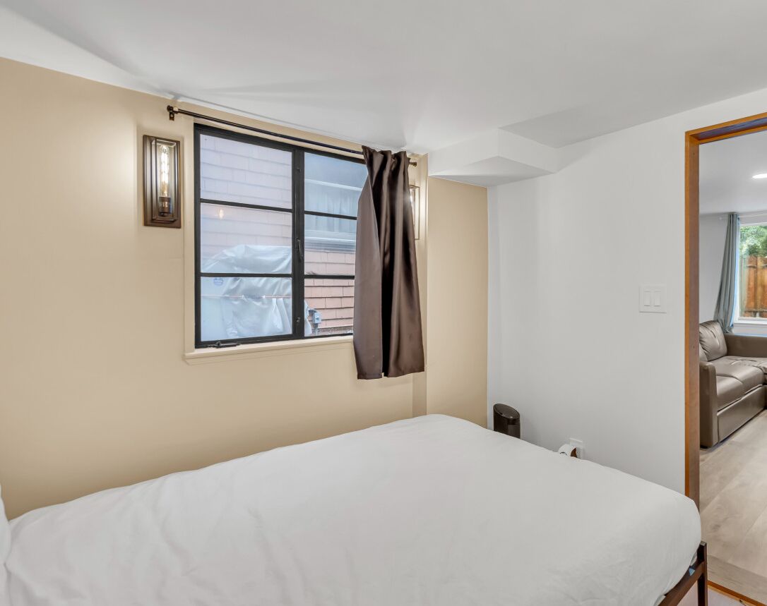 Un dormitorio con cama, ventana con cortinas, luz empotrada en la pared y vistas a un balcón con sofá.