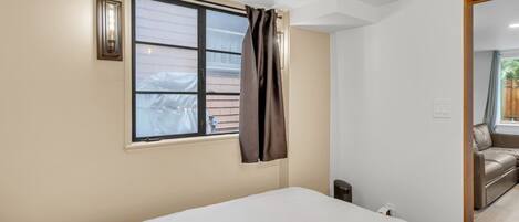 Un dormitorio con cama, ventana con cortinas, luz empotrada en la pared y vistas a un balcón con sofá.