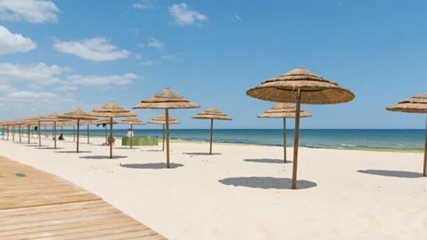 A beach with a wooden walkway and thatched umbrellas.