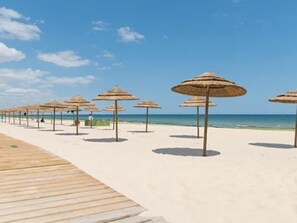 A beach with a wooden walkway and thatched umbrellas.