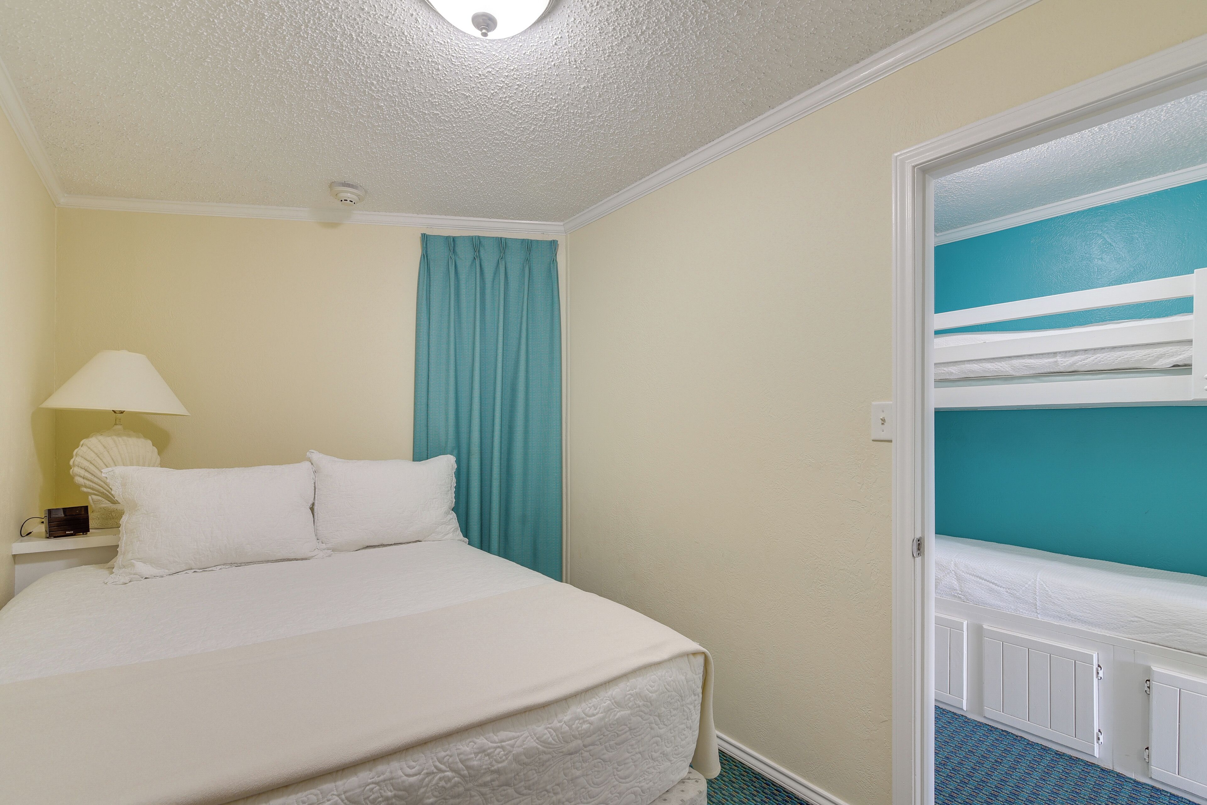 Een hotelkamer met een bed, nachtkastje, lamp, raam met gordijnen en een stapelbed.