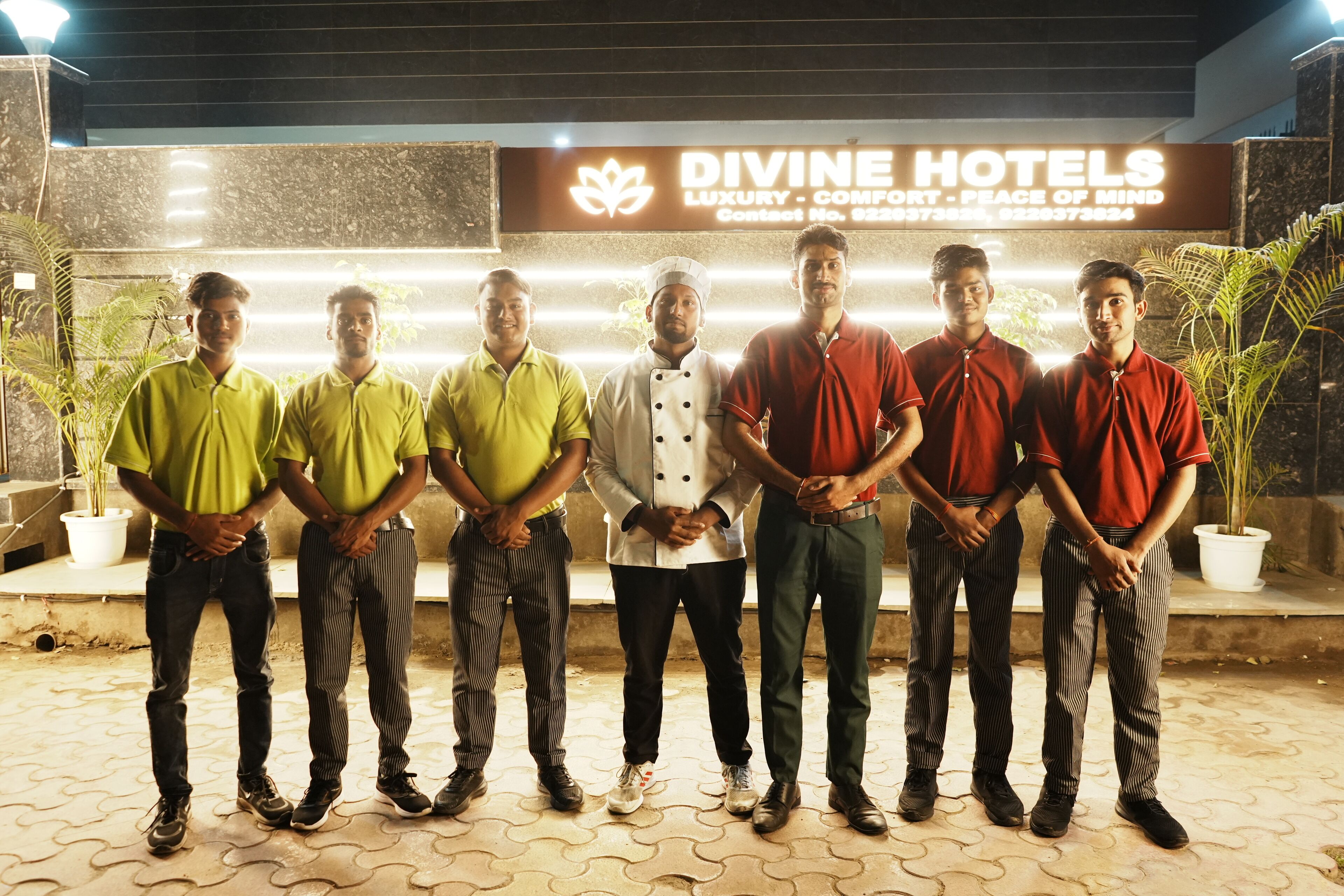 A group of people standing in front of a sign for Divine Hotels, which advertises luxury, comfort, and peace of mind.