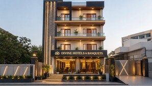 A multi-story hotel with a modern design, featuring balconies, a well-lit entrance, and a sign for 'Divine Hotels & Banquets.' - Divine Hotels & Banquets (Noida)