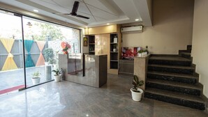 A reception area with a reception desk, a staircase, and potted plants. - Divine Hotels & Banquets (Noida)